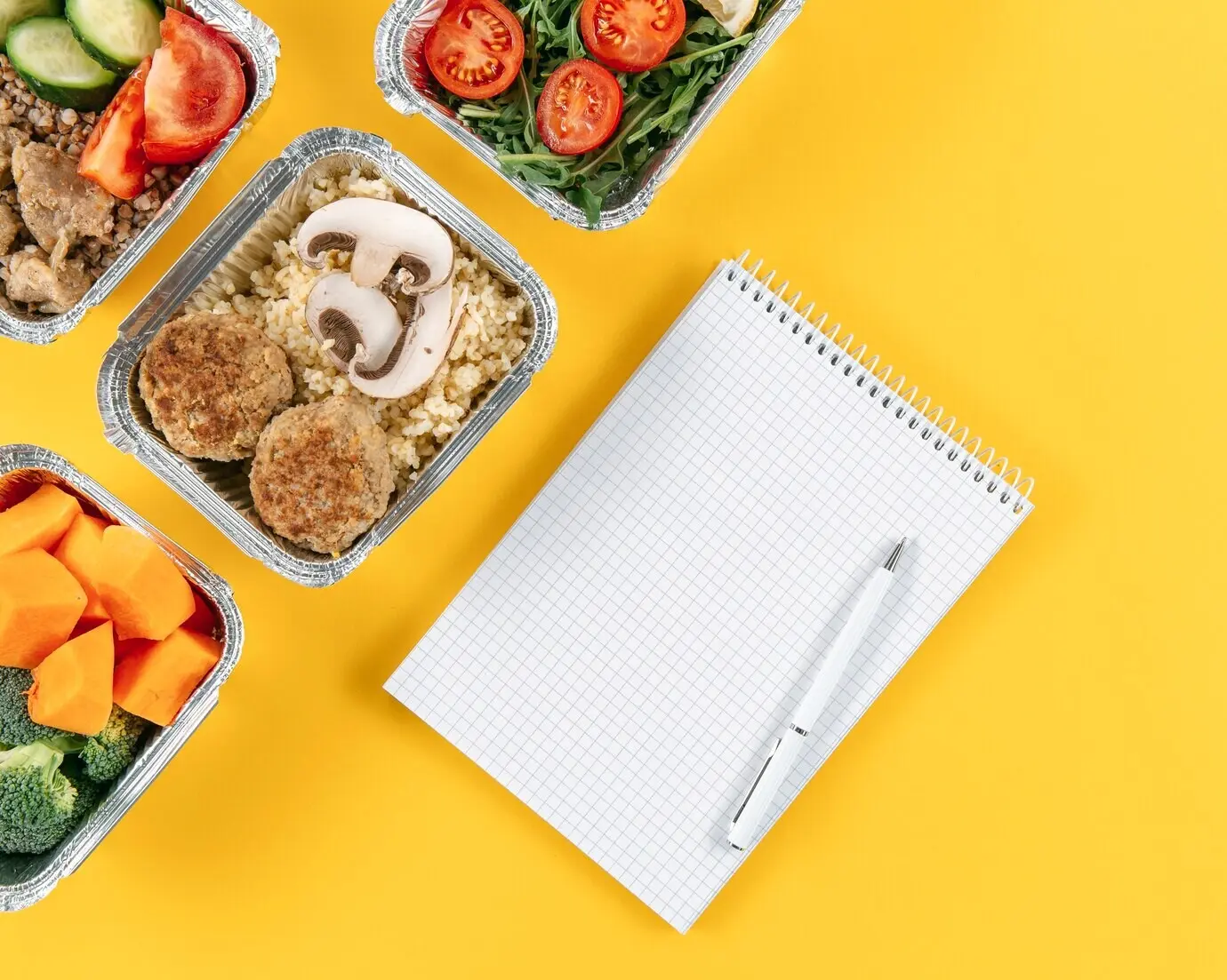 Draufsicht auf ein Notizbuch mit Stift und Mahlzeiten in Auflaufformen